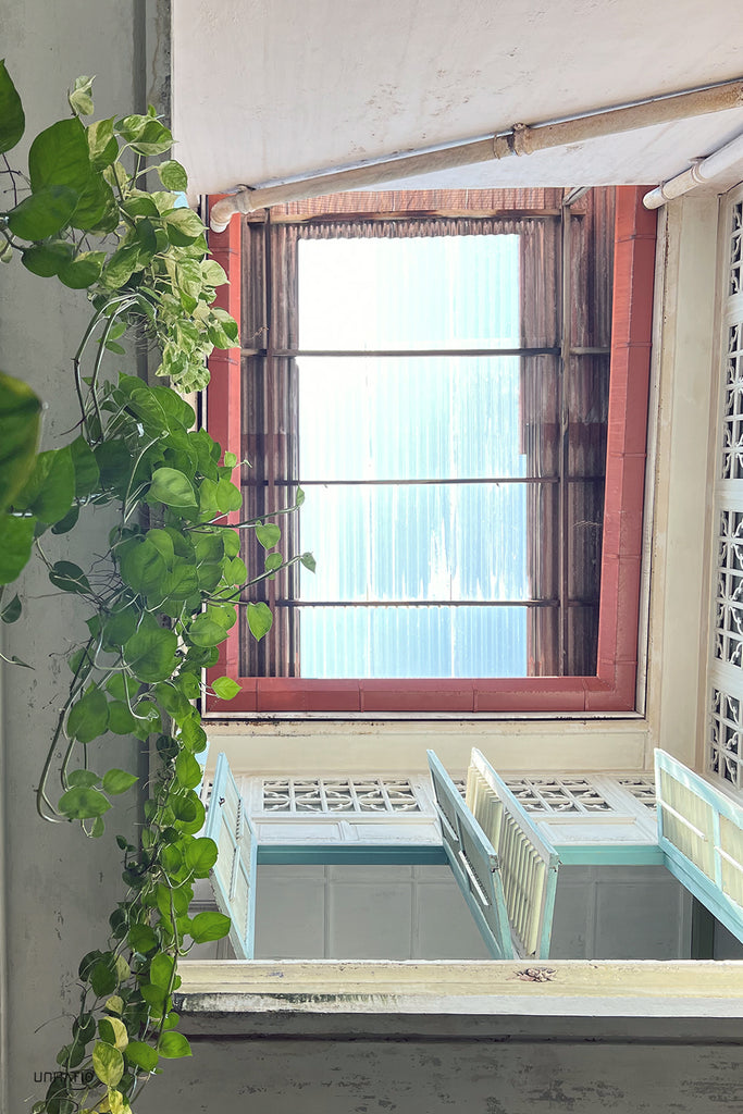 Vertical perspective inside Melaka's heritage cafe, white ornate shutters open to reveal a bright skylight.
