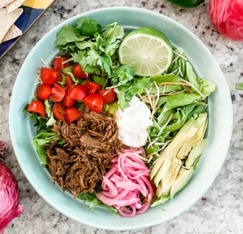 Blue bowl with lettuce, tomatoes, lime, and shredded beef