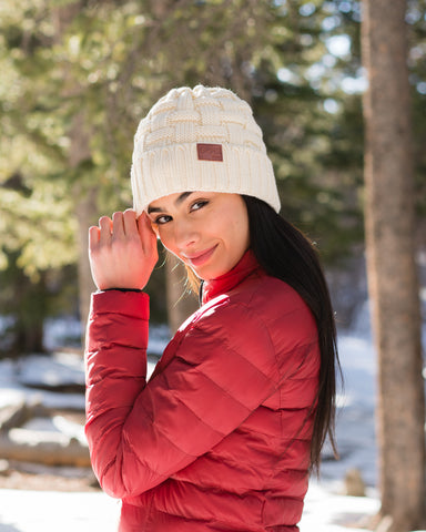 Woman in a red coat wearing Gobi Heat Crest beanie in a snowy forest