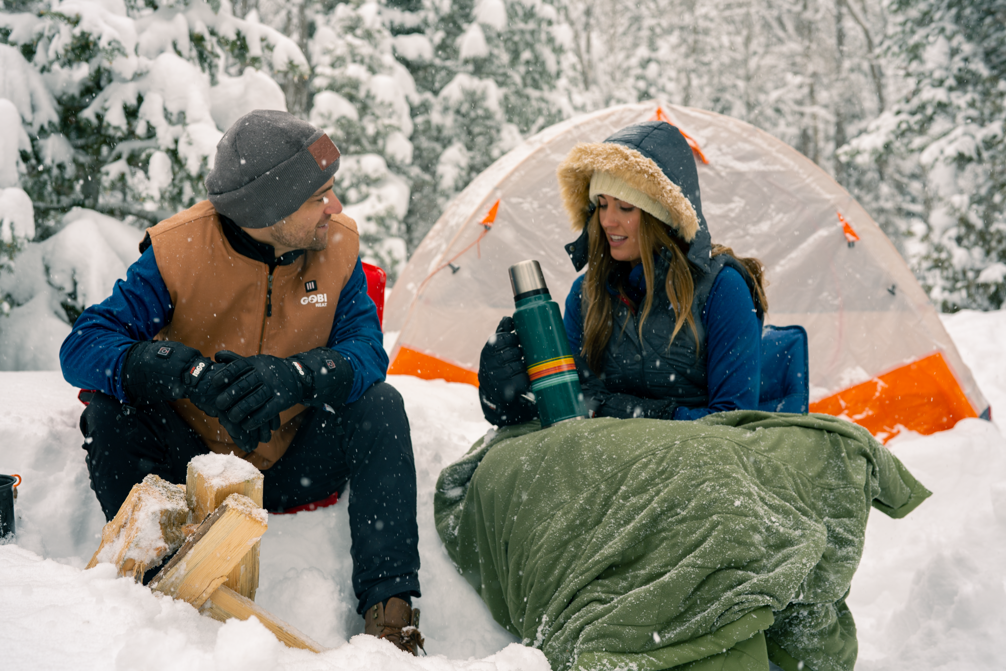 Young couple staying warm at a intery and snowy campsite using their Gobi Heat Zen Heated Blanket