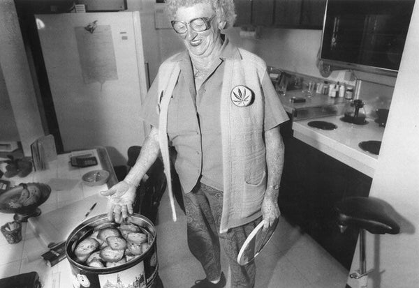 Mary Jane Rathburn, an elderly woman, stands in her kitchen showing off food in a crockpot with a marijuana leaf pin visible on her shirt