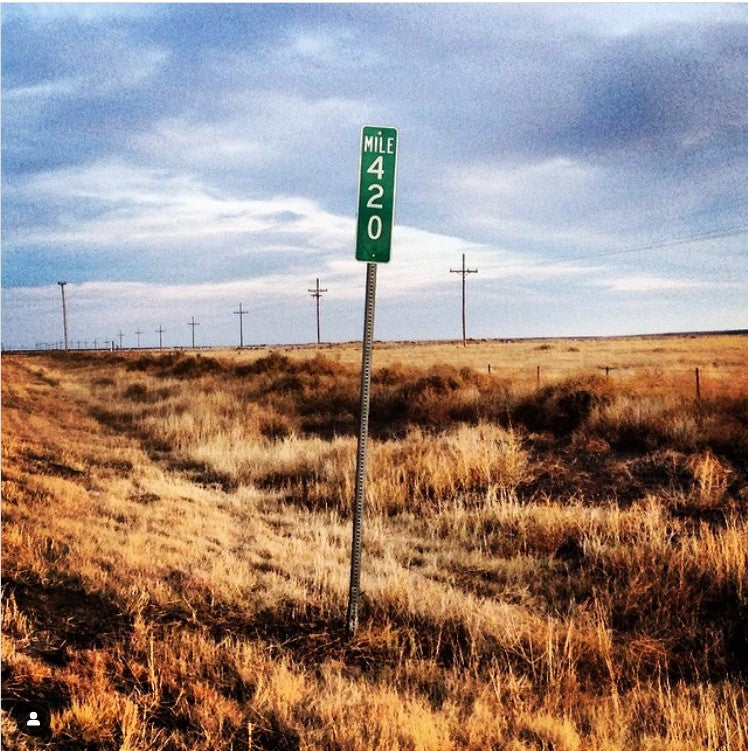 A highway mile marker reading "420" surrounded by prairie grass, with telephone towers in the background.