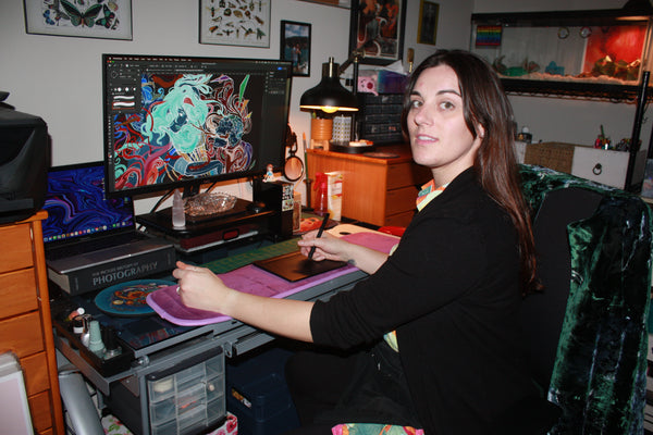 courtney hannen, a woman with brown hair, sits at her computer desk working on a digital art piece
