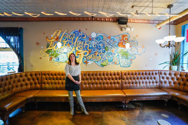 Courtney Hannen standing in front of a mural she painted in a restaurant 