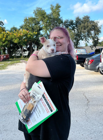 Woman holds recently adopted white puppy in parking lot with Mighty Paw Yak Chew.