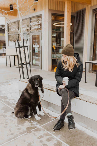 Woman sits outside in the winter with a coffee and her long-haired black dog on a Mighty Paw Leash.