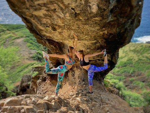 Two women doing dancer pose under a rock archway