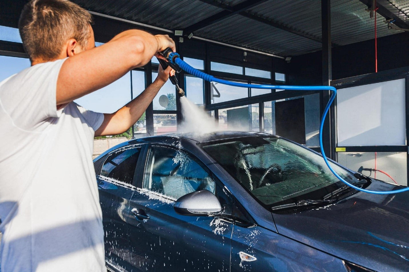 A man washes his car at a self-service car wash using a hose with pressurized water car carez blog image carcarez blog