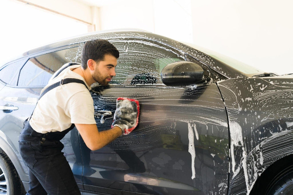 Attractive young latin man washing a customer's car with a car wash glove and foam at car wash car carez