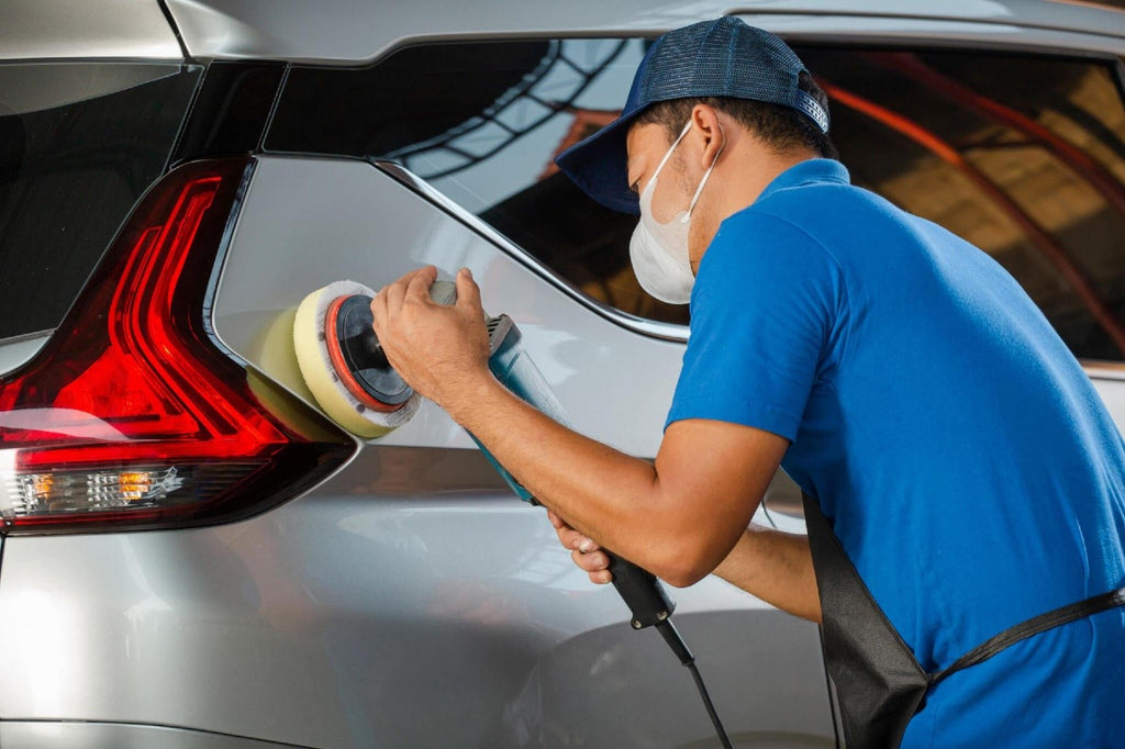 Car detailing and polishing concept. Professional car service male worker with orbital polisher, polishing metallic car in auto repair shop