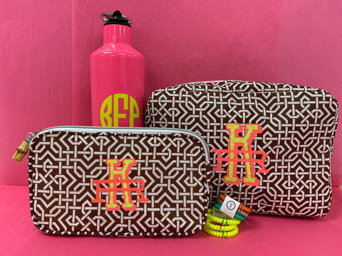 Two make-up bags with embroidery initials, bright yellow and pink in color. Behind them is a large, pink water bottle with initials in bright yellow.