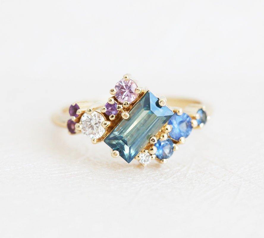 The Lila Teal Blue Sapphire Cluster Ring is a cornucopia of gemstones including sapphires, amethysts, and diamonds.