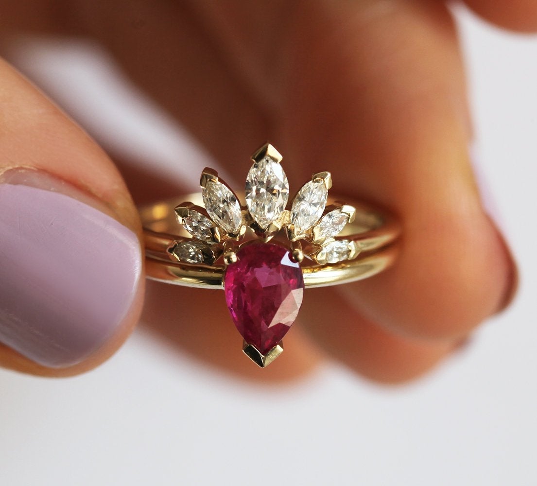 A manicured hand holding the Korina Natural Ruby Engagement Set with Diamond Crown Ring by Capucinne.