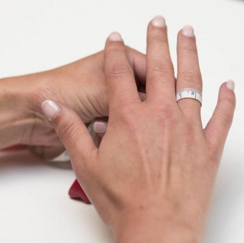  A person showing how to measure ring size at home using your finger circumference and a measuring tape.