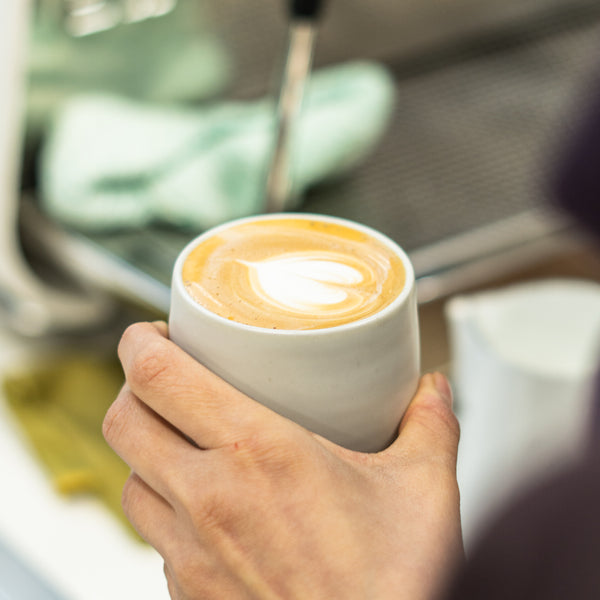 Hand holding cup of specialty coffee with latte art love heart 