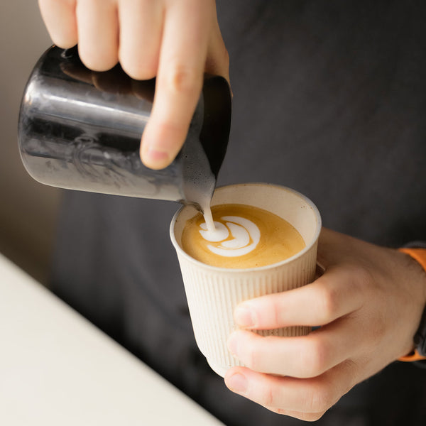 Person doing latte art in a beige cup