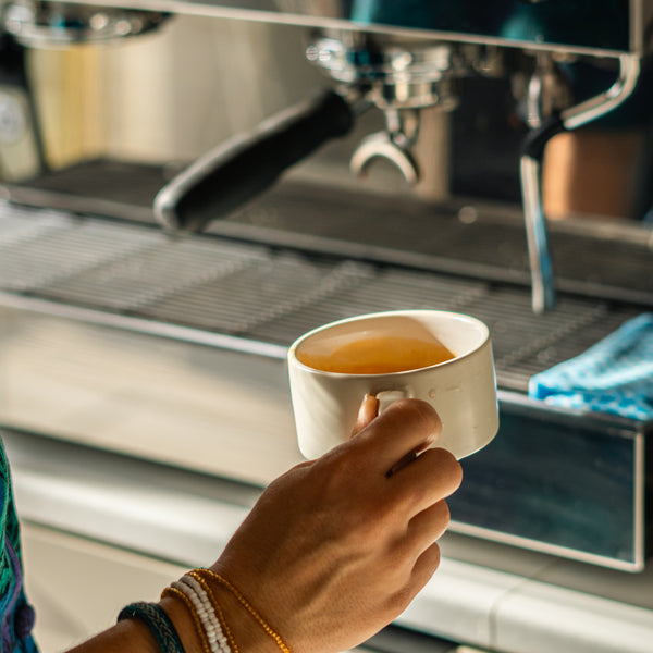 Person holding coffee cup in front of an espresso machine