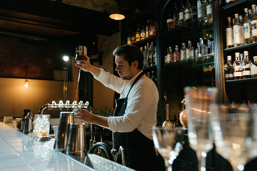 The man at the bar pours whiskey into a unbreakable tritan glass