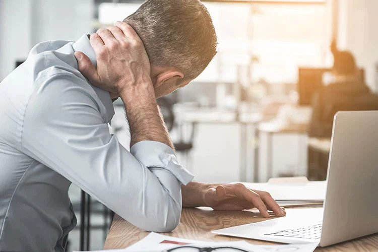 man with a laptop touching his neck to relieve pain