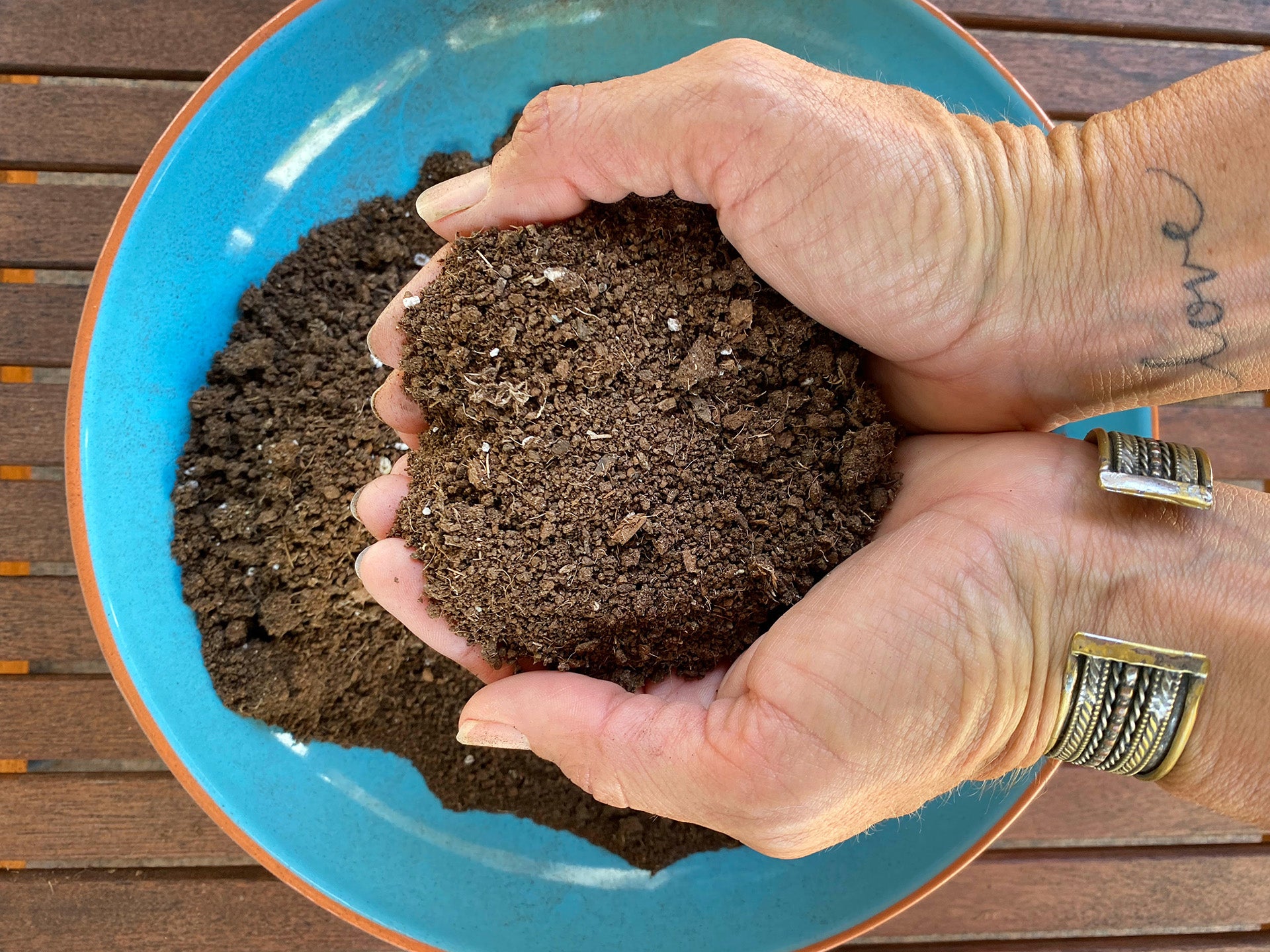 Two hands lifting potted soil from a bowl