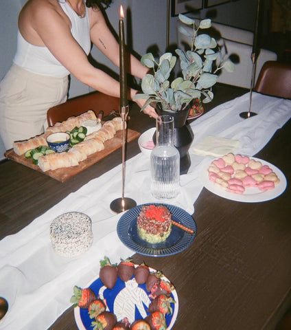 film photo of galentine's night dinner with girl setting up a table with candles, desserts, and flowers