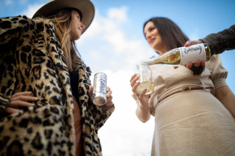 two ladies drinking wine from a can and jar