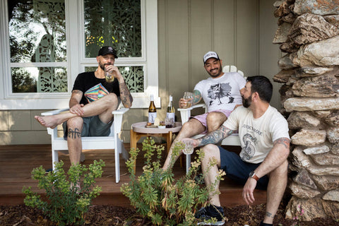 3 men dinking wine out of jars on a front porch 