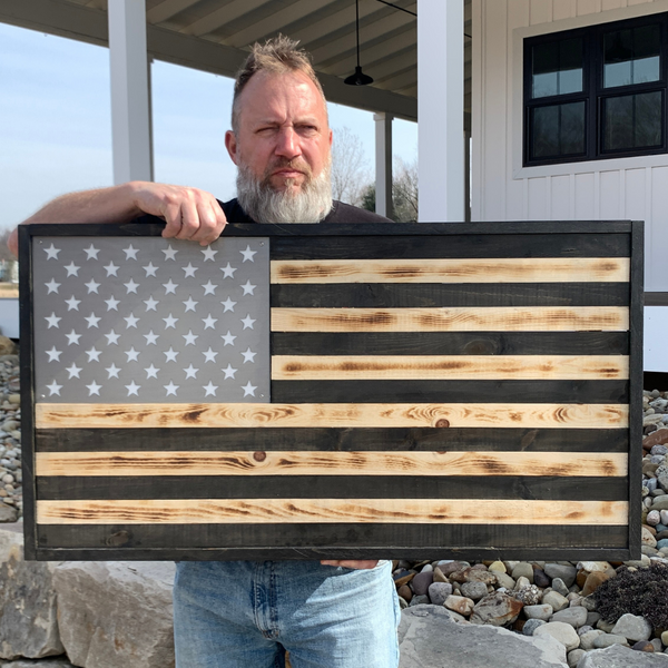 A middle aged American man with a stern facing holding a big, beautiful wooden US flag with a metal insert for the stars. 
