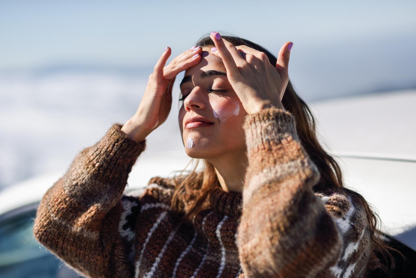 a girl wearing a sweater applying sunscreen outside winter skincare tips moisture loss retain moisture fatty acids dry skin skincare routine