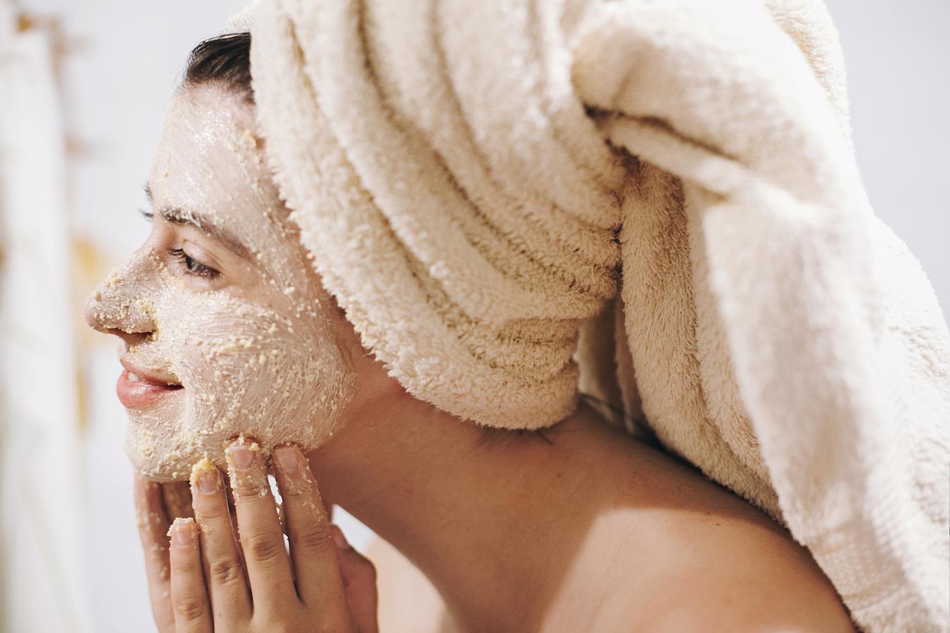 girl with a towel on her head applying a face scrub vitamin c serum layer skincare products applying skincare skin care products