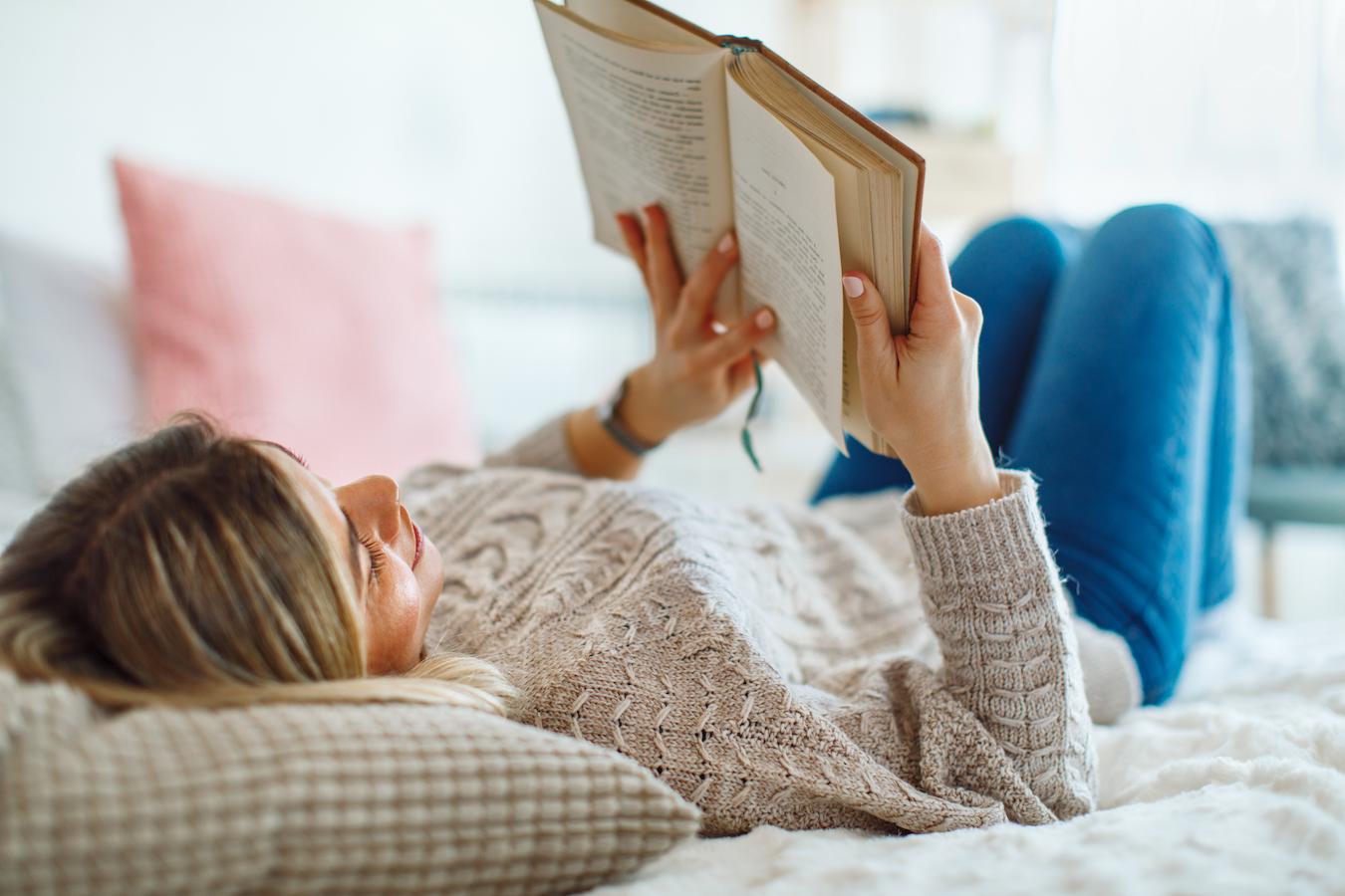 woman reading a book on her bed creative side prioritize tasks intellectual wellness encourages learning