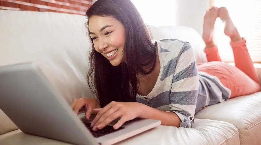 smiling-asian-woman-couch-using-laptop 1.webp__PID:6a40145e-844a-4c49-bb62-3f02da2bbdb6