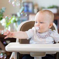 baby using pacifier clip playing with bubbles