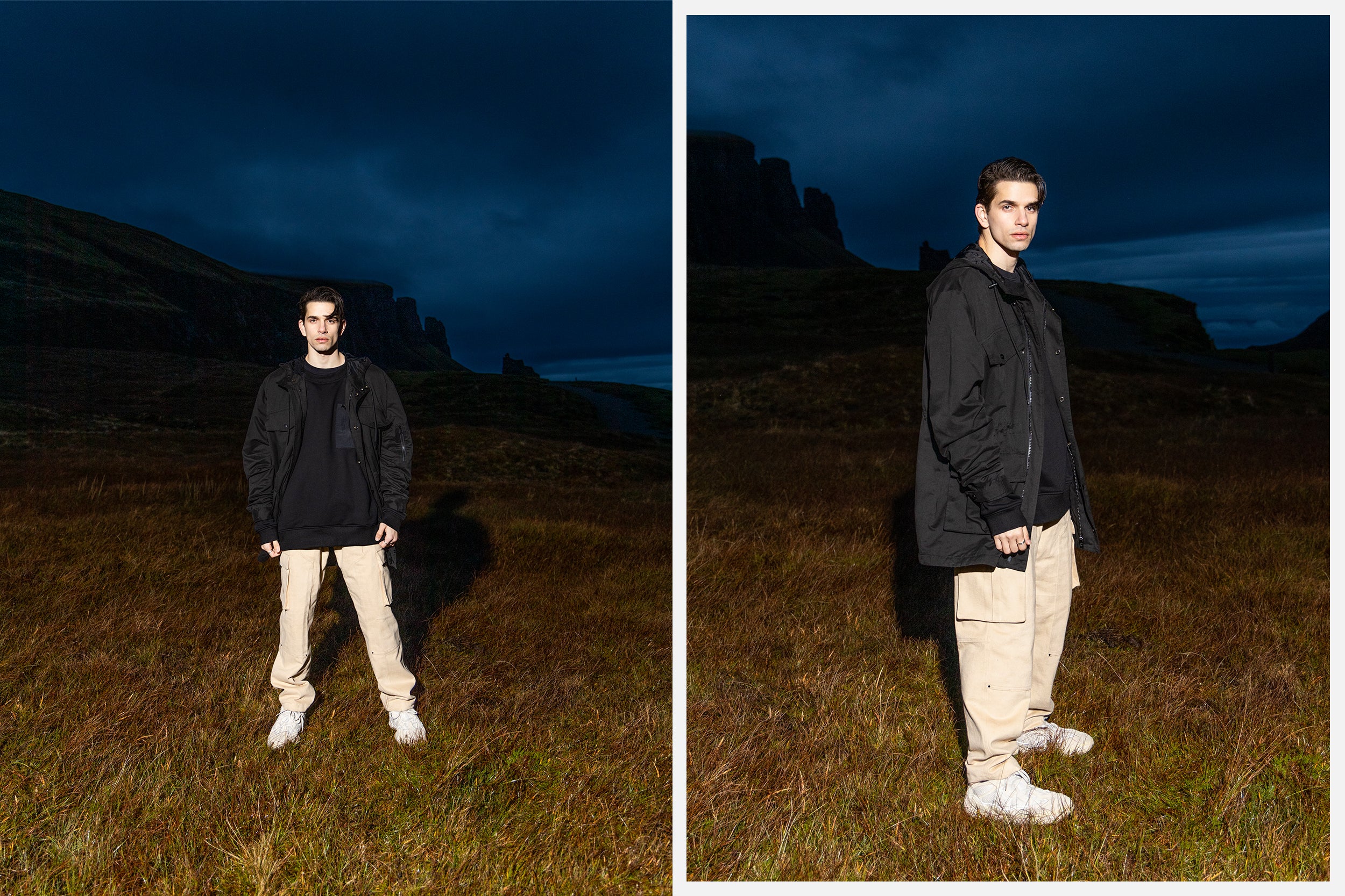 A male model in black jacket and sand cargo pants stand atop the Isle of Skye.