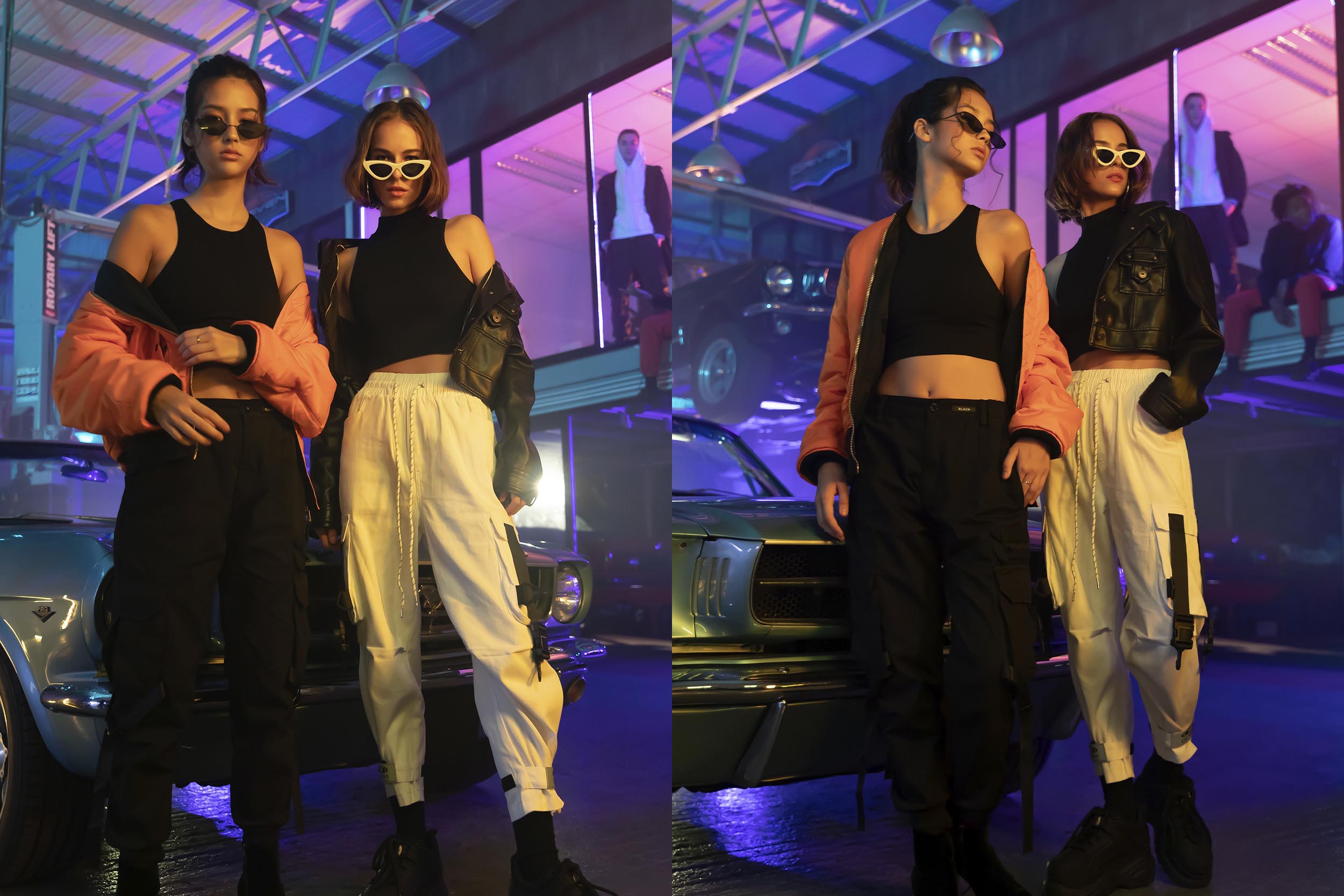 Two female model in cargo pants and jackets standing next to a car.