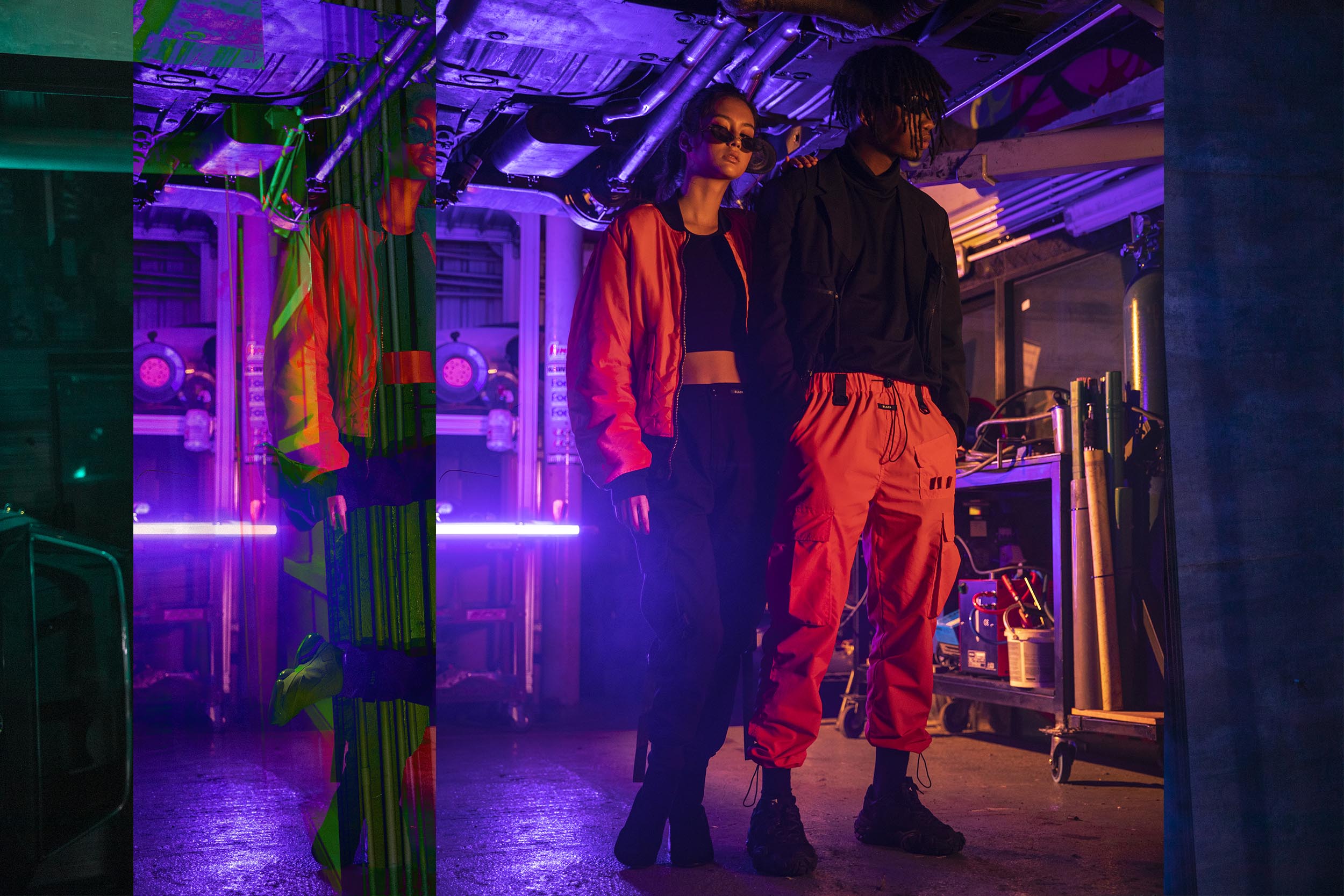 A male model wearing orange cargo pants and a black jacket standing beside a female model in black cargo pants and an orange jacket.