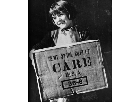 Black and white image of young girl smiling and holding a CARE sign