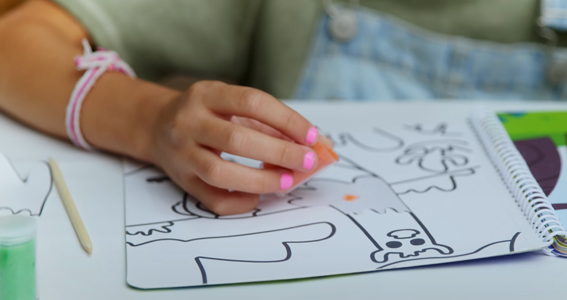Mãos de criança aplicando areia colorida sobre um desenho adesivo de um animal.