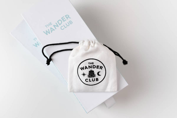 A white bag sitting on top of a box, everything branded with The Wander Club, some of the best travel basket gift ideas