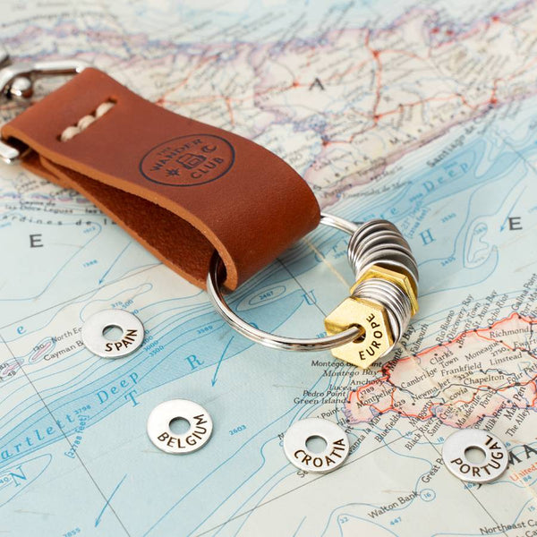 A brown leather Wanderchain with several Travel Tokens from The Wander Club, some of the best gifts for map lovers