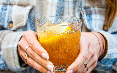 Holding a tumbler glass of a gold-coloured cocktail with lemon