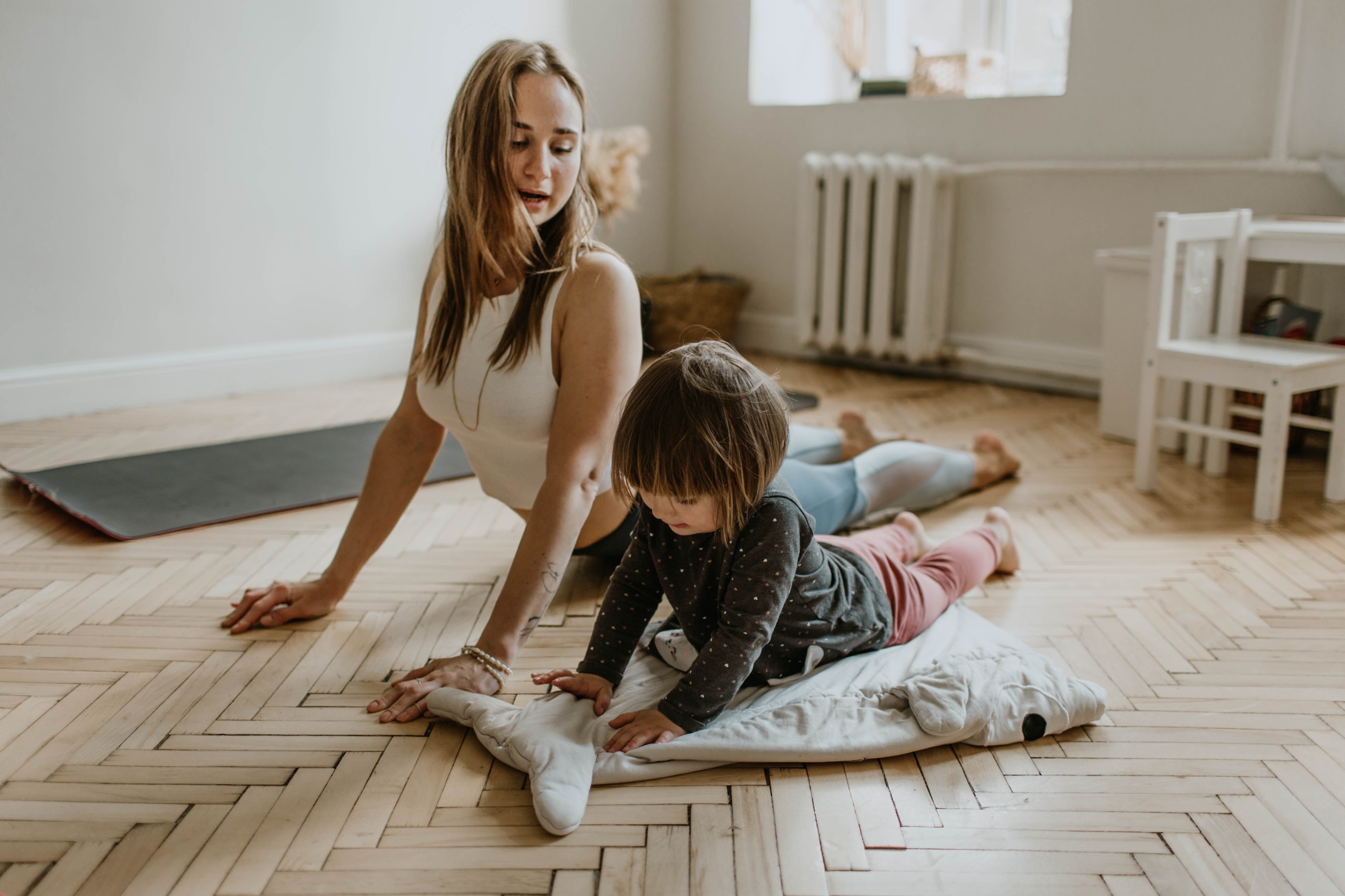 Une mère et sa fille faisant du yoga sur le sol de leur salon.