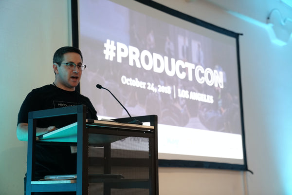 A man in a black shirt and specs standing in front of a podium