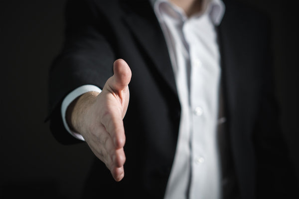 A man in a black overcoat and a white shirt extending his hand for  shaking hand 