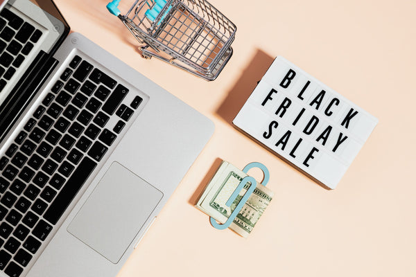 A keyboard, shopping cart, dollars, and a placard with Black Friday Sale written on it