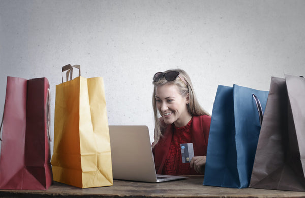 A satisfied customer amidst shopping bags sitting with a laptop to write the review