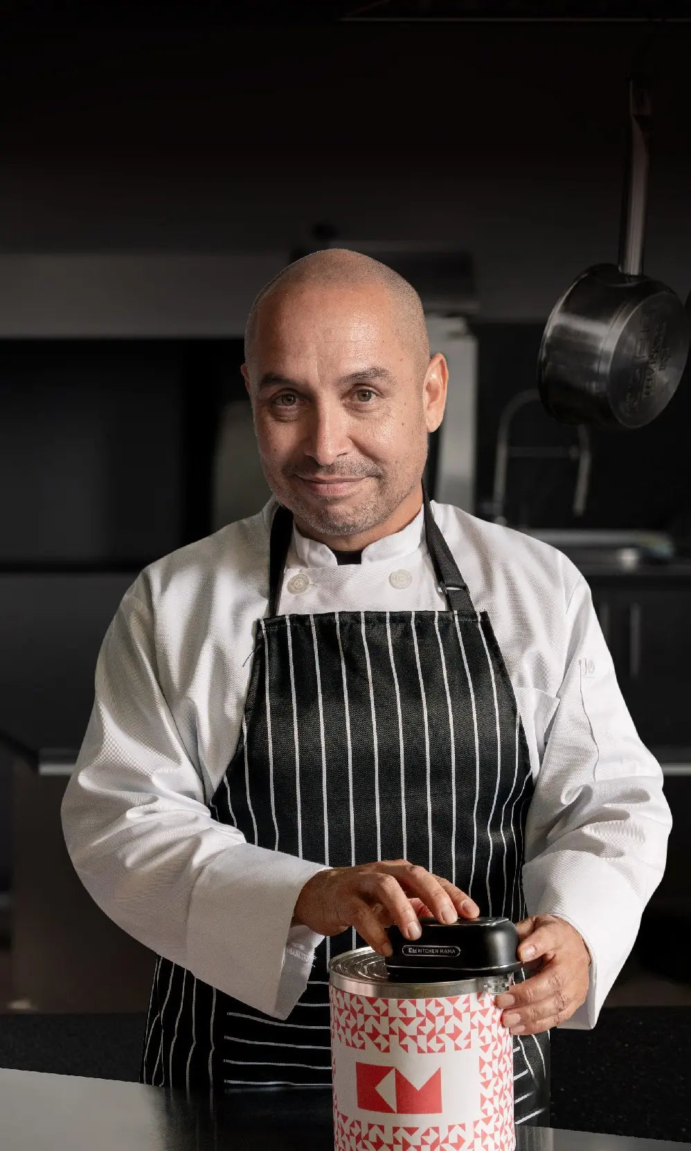 A chef in a black and white striped apron is opening a patterned container in a modern kitchen setting.