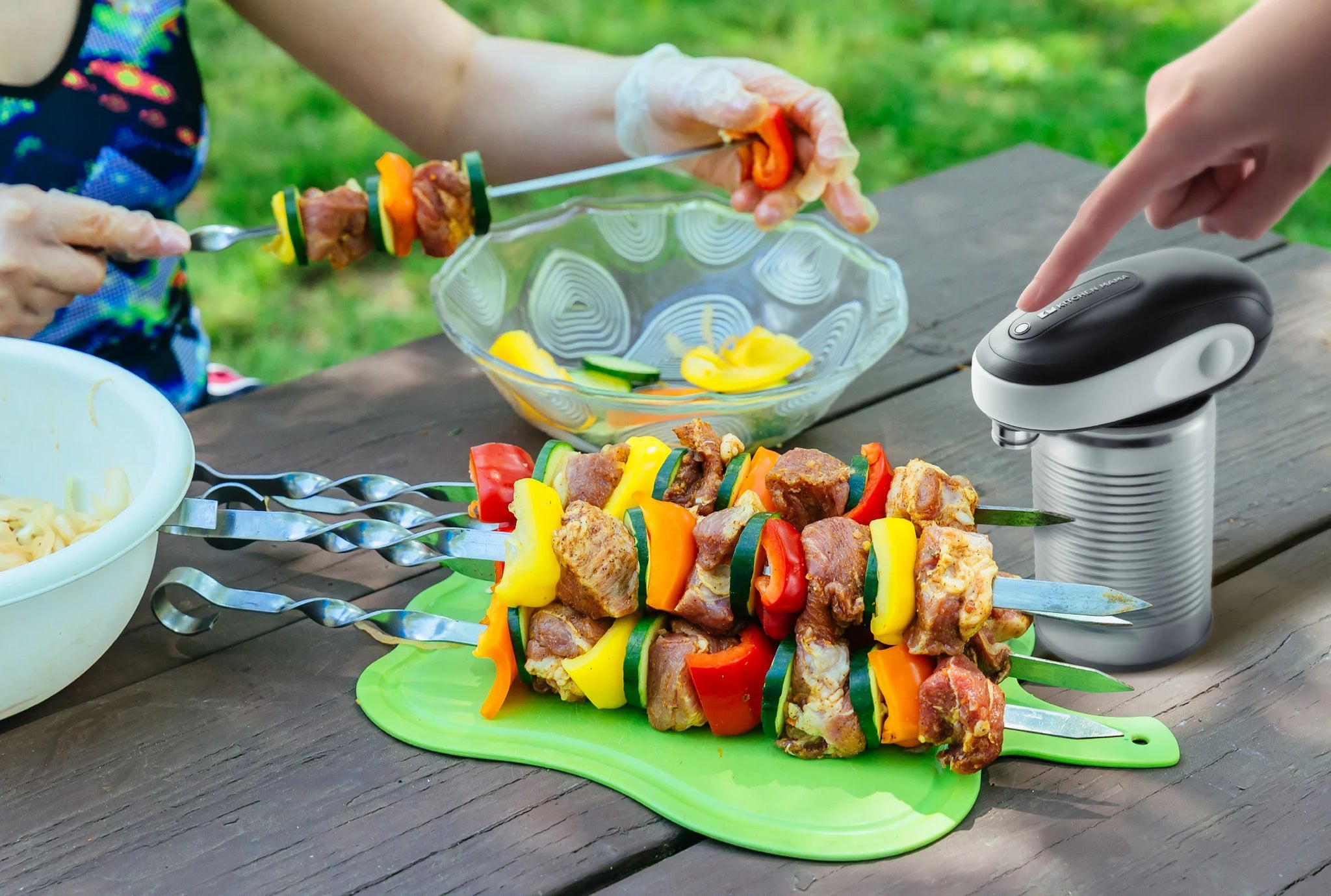 A person preparing colorful meat and vegetable skewers outdoors with the Kitchen Mama One-to-Go can opener placed on a table next to a can and cutting board.