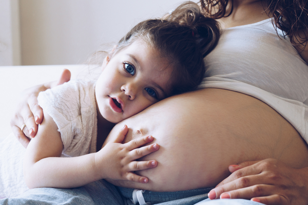 a pregnant woman holding her young daughter in her arms