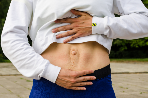 A woman gently supporting her abdomen with both hands, showing awareness of diastasis recti